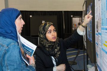 Photo of researcher explaining her poster to a colleague.
