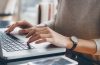 Close-up photo of a woman's hands typing on a laptop keyboard