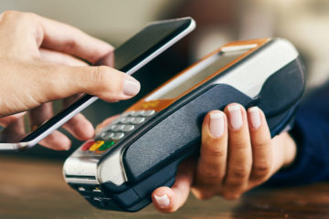 someone paying with a phone, hovering a smartphone over handheld credit card reader