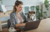 Photo of a woman on a laptop with her dog looking at the screen