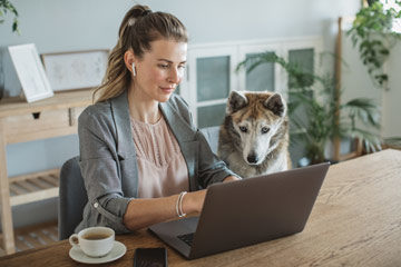 Photo of a woman on a laptop with her dog looking at the screen