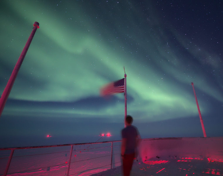 Photo of Allen Foster standing on the station deck looking out at the auroras overhead in the night sky