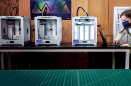 Case Western Reserve Sears think[box] employee Ainsley Buckner works on a laptop next to 3D printers