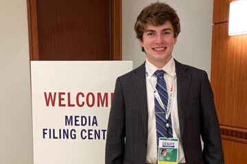 Photo of Nathan Lesch in front of a sign that says "welcome media filing center"