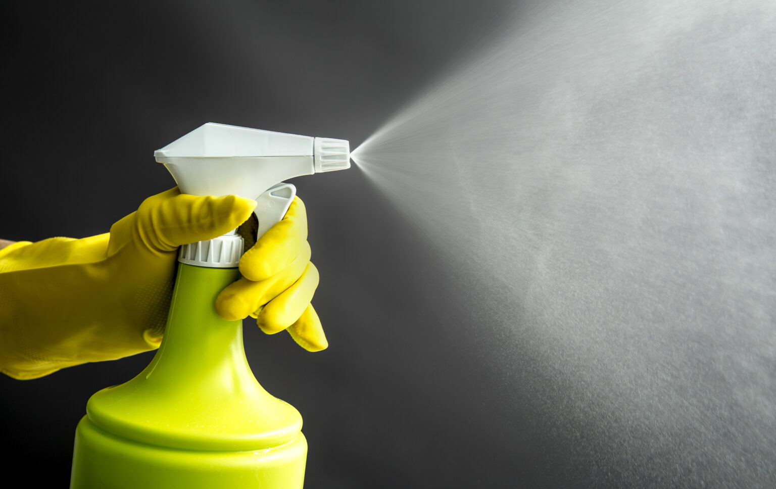Woman wearing yellow rubber gloves using green spray bottle and